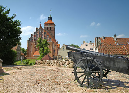 The castle square in Reszel, Poland. An old cannon in the foreground and a church in the background. A sunny summer view.