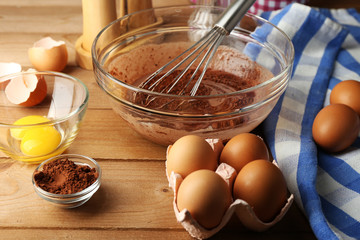 Preparation cream with eggs and cocoa in glass bowl on wooden background