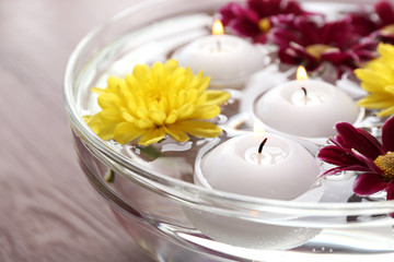 Bowl of spa water with flowers and candles on wooden table, closeup