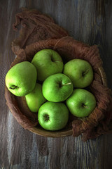 Green apples in bowl with fabric on wooden table, top view