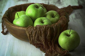 Green apples in bowl with fabric on wooden table, closeup