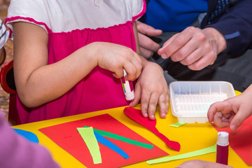 children and adults hands glue colored paper on application mast