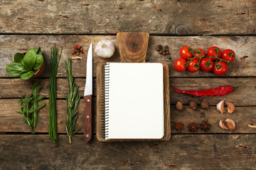 Open recipe book with fresh herbs, tomatoes and spices on wooden background