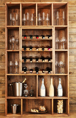 Shelving with wine bottles with glasses on wooden wall background © Africa Studio