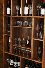 Shelving with wine bottles with glasses on wooden wall background
