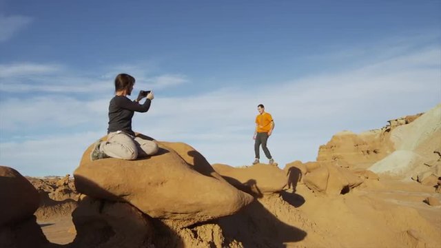 Medium shot of woman photographing man jumping on rock in Goblin Valley / Goblin Valley State Park, Utah, United States, 