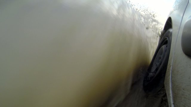 Driving in the rain on a road with puddles and muddy water