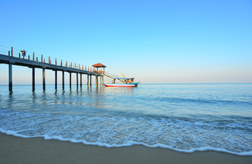 Beautiful sunset at tropical beach with a bot end of jetty