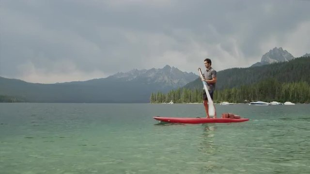 Wide shot of young man paddleboarding on lake / Redfish Lake, Idaho, United States