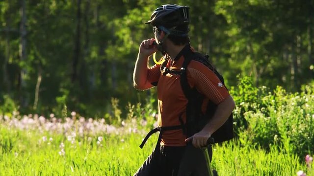 MS TU Bike rider with artificial limb taking a break and drinking water from backpack on meadow, then riding off / American Fork Canyon, Utah, USA