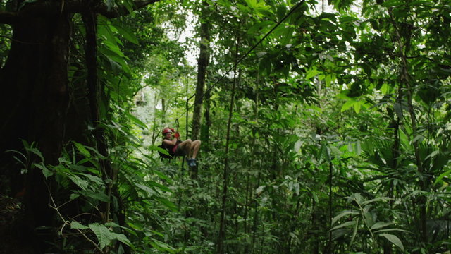 Medium panning shot of woman ziplining to landing in rain forest / Quepos, Puntarenas, Costa Rica
