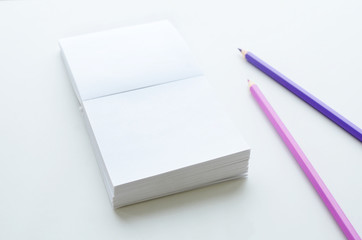 Empty note paper block and two pencils on light background