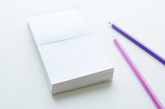 Empty note paper block and two pencils on light background