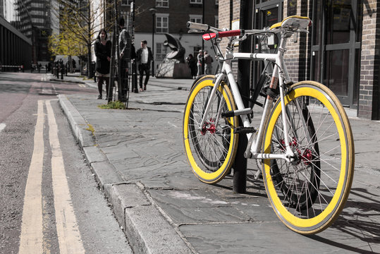 Modern single gear bycicle with yellow tyres locked to a lamp