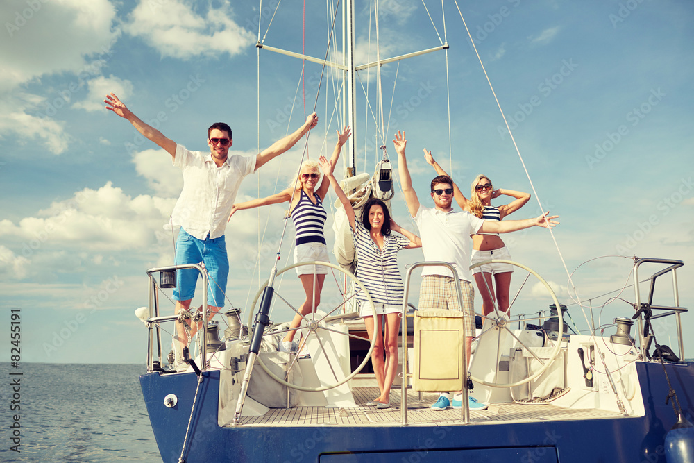 Wall mural smiling friends sitting on yacht deck and greeting