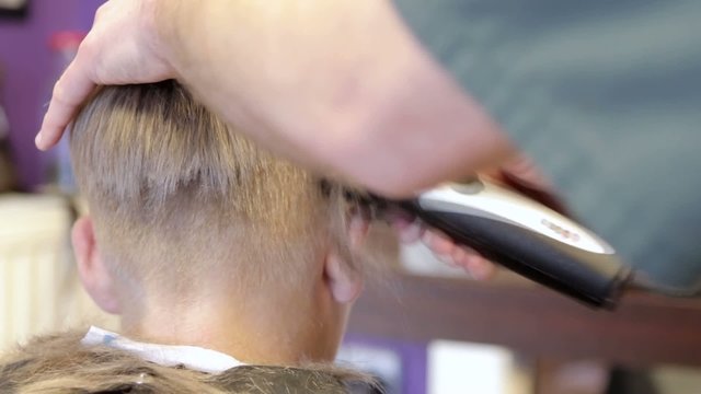Hairdresser cutting hair of young boy by electric trimmer