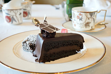 Slice of thick dark chocolate cake on gold trimmed plate with ot