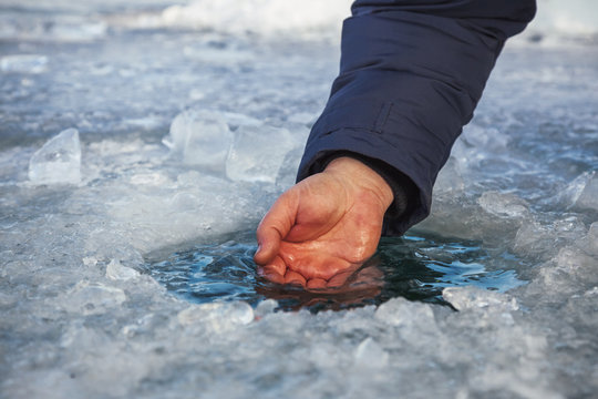 Male hand scoops water from the hole of the lake