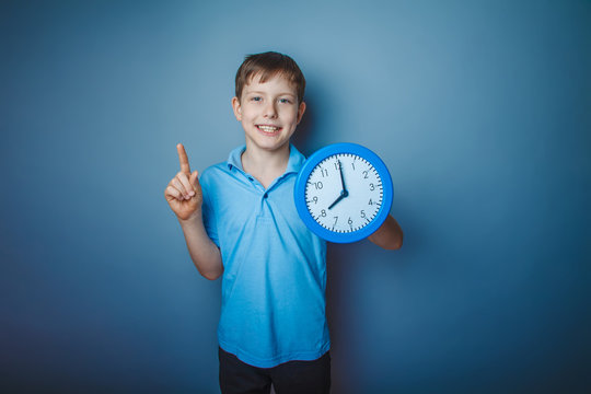 teenager boy brown European appearance holds a watch on gray bac