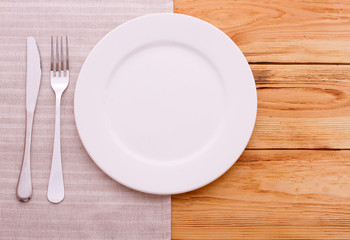 Empty plates, cutlery tablecloth on wooden table for dinner,