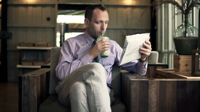 Young businessman reading newspaper and drinking cocktail