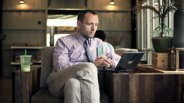 Young businessman with smartphone and laptop sitting in cafe 
