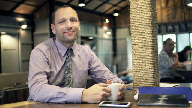 Portrait of young, happy businessman drinking coffee in cafe 
