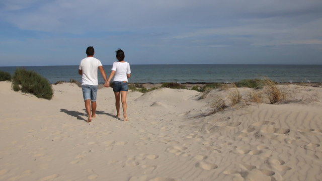 Young man and woman holding hands and walking on the beach in sunny day - Powered by Adobe