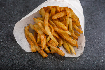 Potatoes fries in white paper bag on a black background