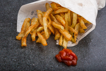 Potatoes fries in white paper bag on a black background