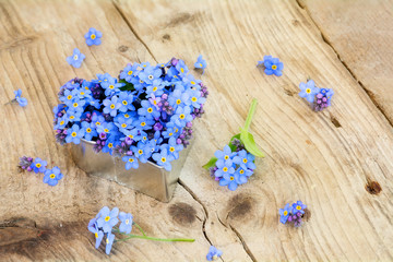 forget-me-not flowers in a silver heart shape on rustic wood