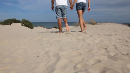 Young couple holding hands and walking on the beach in sunny day