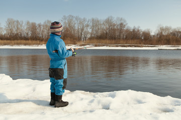 Fototapeta na wymiar Boy fishing with rod on river in winter.
