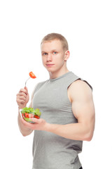 Young happy muscular man eating a salad over white background.