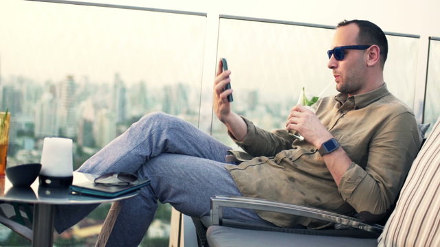 man with cocktail taking selfie  sitting on terrace