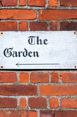 Sign for 'The Garden' on a brick wall background