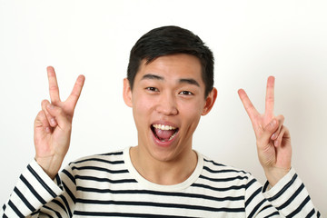 Laughing young Asian man giving two victory signs and looking at