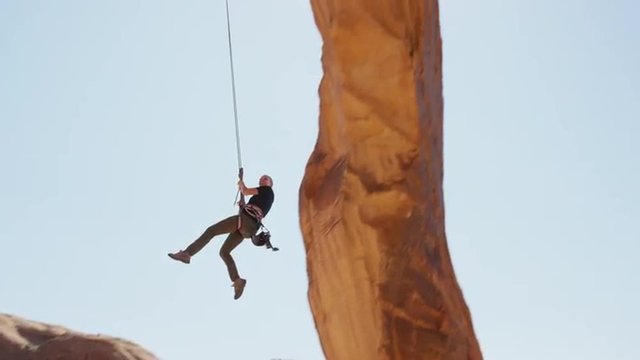 Slow motion wide tracking shot of woman swinging from arch / Corona Arch, Moab, Utah, United States