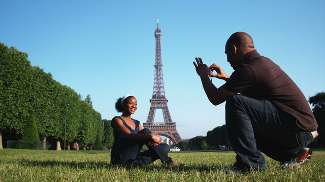 man taking a photo of a woman on the lawn in front of the Eiffel tower