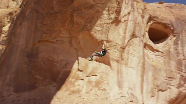 Wide tracking shot of man swinging from arch / Corona Arch, Moab, Utah, United States