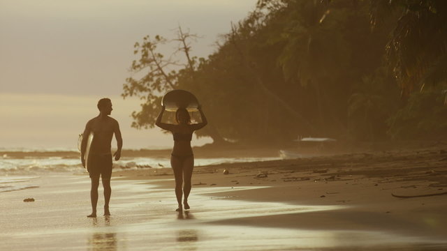 Wide panning shot of couple carrying surfboards on beach / Esterillos, Puntarenas, Costa Rica
