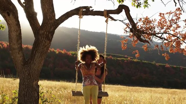 SLO MO MS TD Two teenage girls playing on rope swing on tree in field, South Fork, Utah, USA