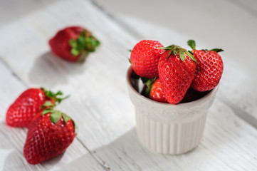 Strawberry in ceramic cup on white wooden background