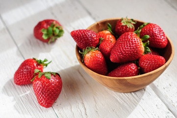 Strawberry in wooden bowl on white wooden background