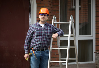 smiling worker in hard hat leaning against metal ladder