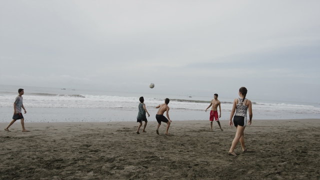 Wide slow motion panning shot of people playing soccer on beach / Esterillos, Puntarenas, Costa Rica