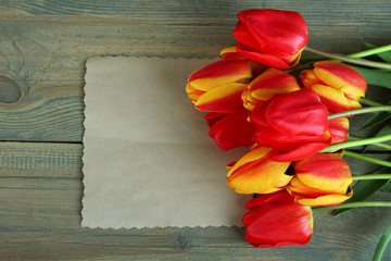 Fresh beautiful tulips and paper on wooden background