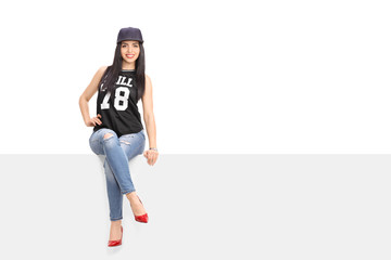 Young woman in hip hop outfit sitting on a billboard