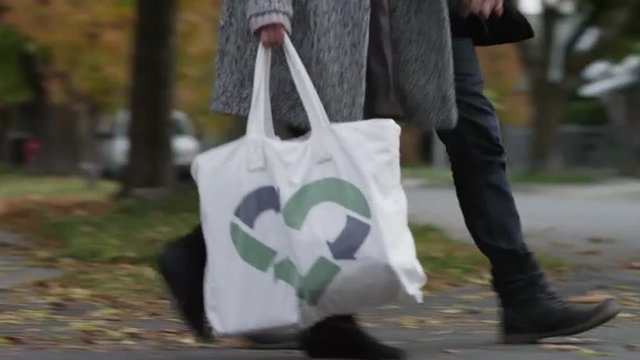 MS TS Young couple walking on sidewalk in Autumn, woman carrying recycling bag, low section / Provo, Utah, USA
