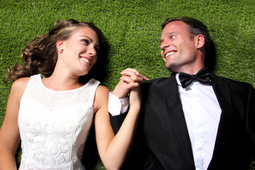 newlywed couple lying on the grass and holding each other hands